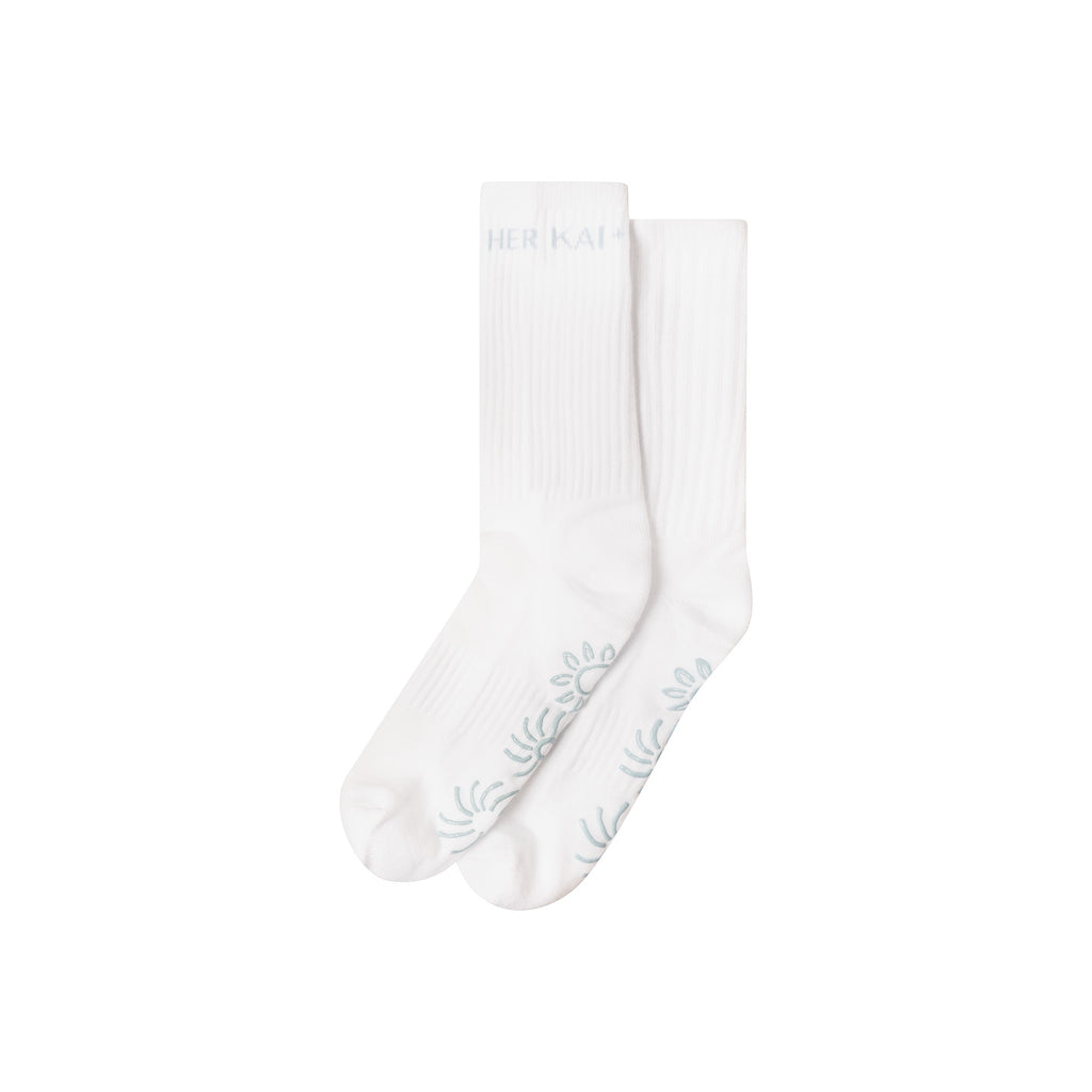 Sol Cotton Socks in White by Her Kai & I. It features a Sun grip design in light blue on bottom of the sock
