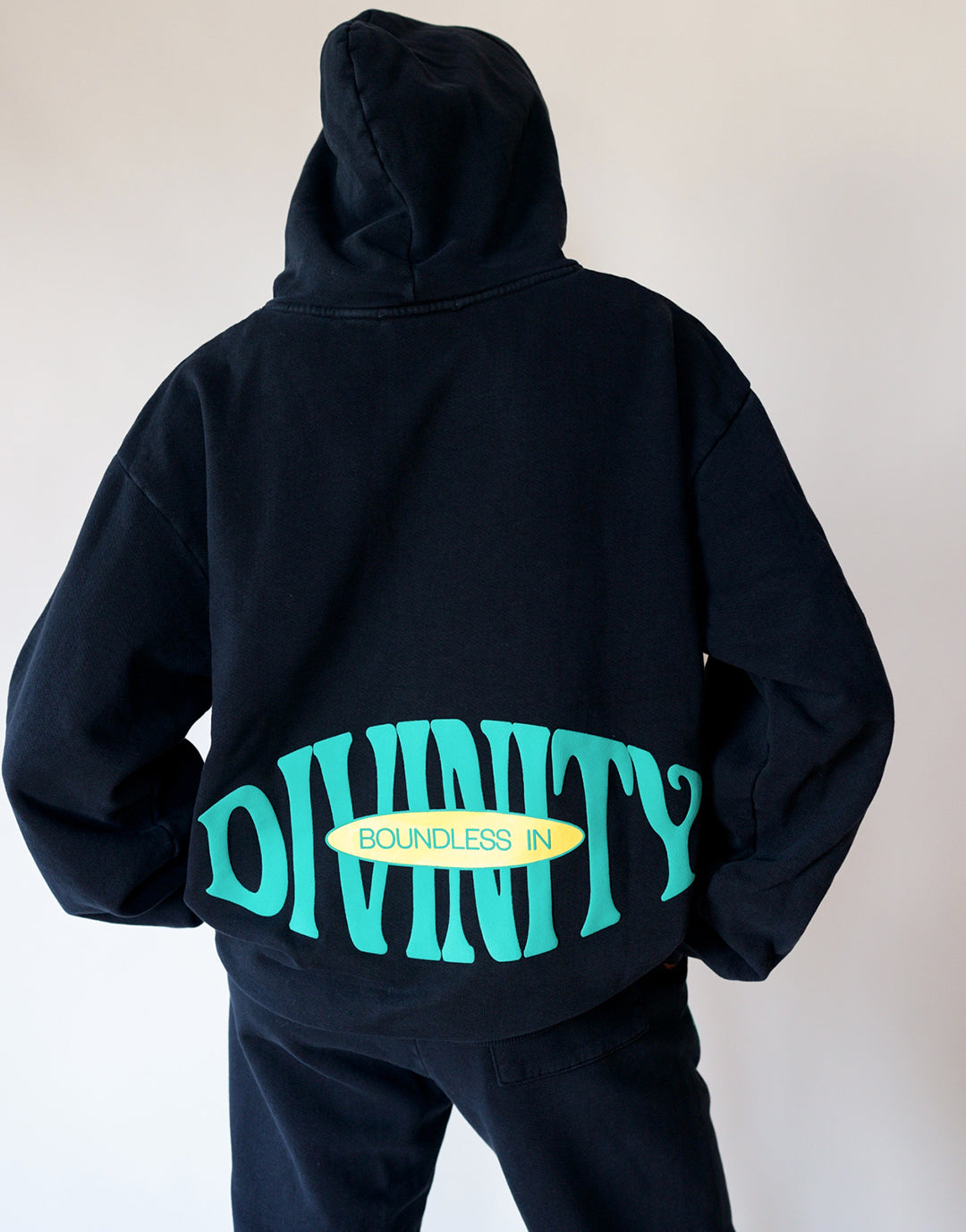 Back View of Model wearing a size Small. Our Boundless in Divinity Hoodie features a Boundless in Divinity Graphic Puff Print.